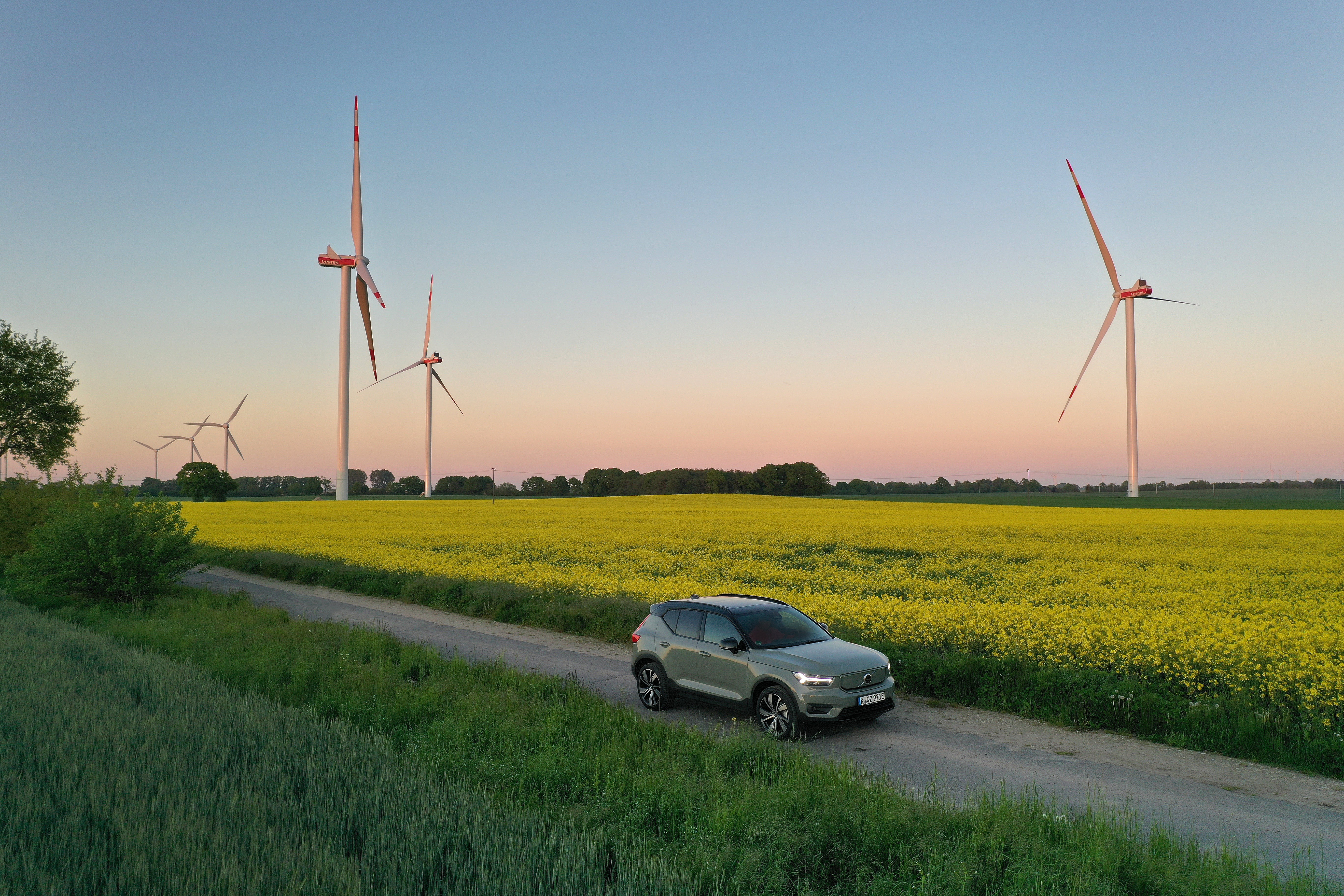 electric car driving on a countryside road with fields and windmills behind it