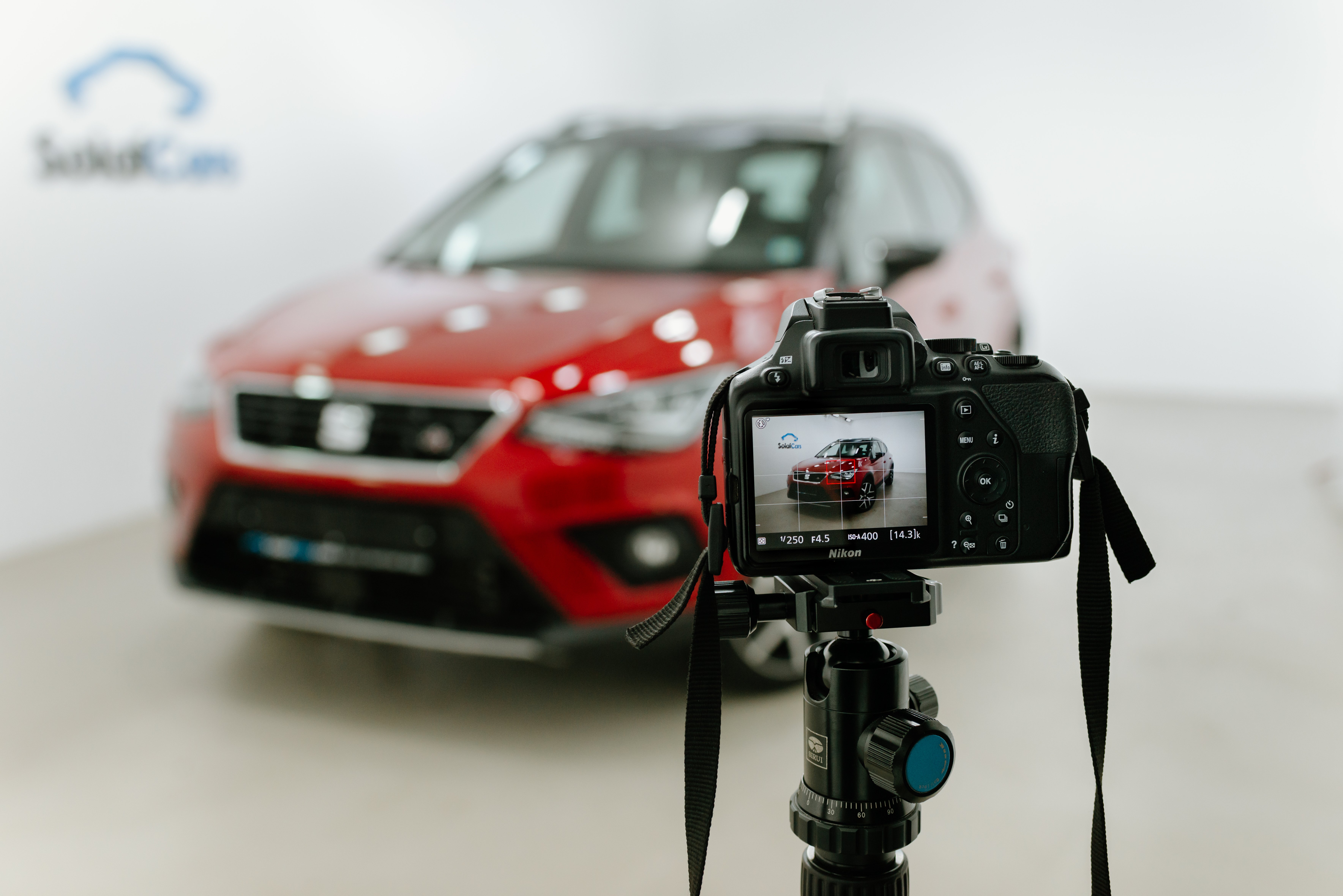 Dslr professional camera placed on a tripod in front of a red car