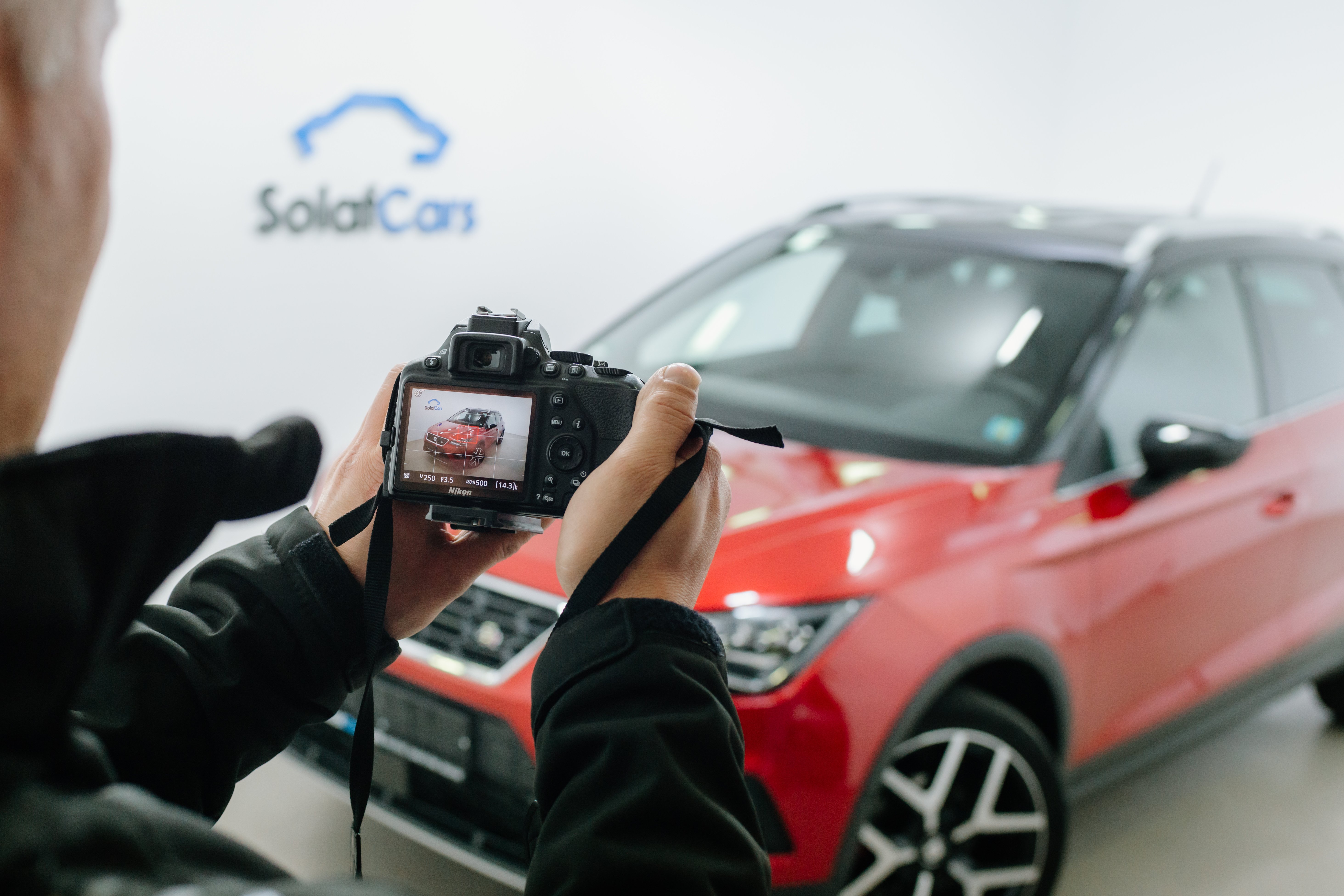Close up of a man taking a photo on a dslr camera of a red car in a photo studio
